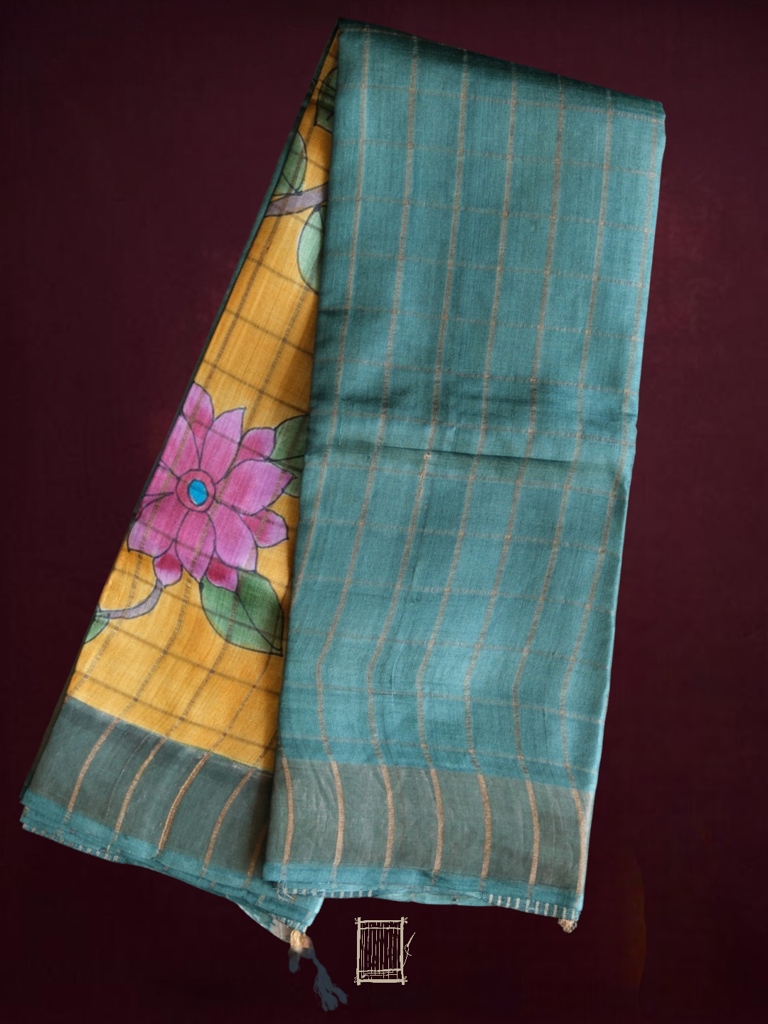 Sea-teal and mustard hand-painted kalamkari tussar silk saree, folded flatlay with pink lotus pallu visible